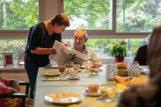 Woonassistent in een huiskamer die de krant leest met een bewoner tijdens een kopje koffie